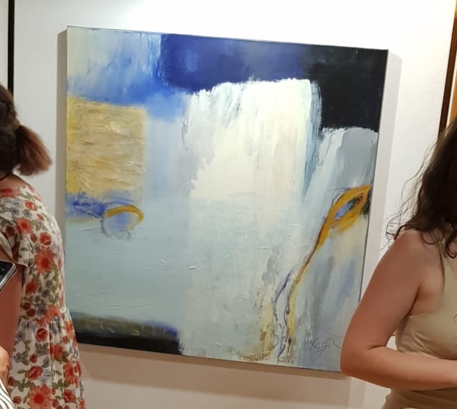 The same painting on the exhibition wall, with two visitors in the foreground standing in front of it and looking at it