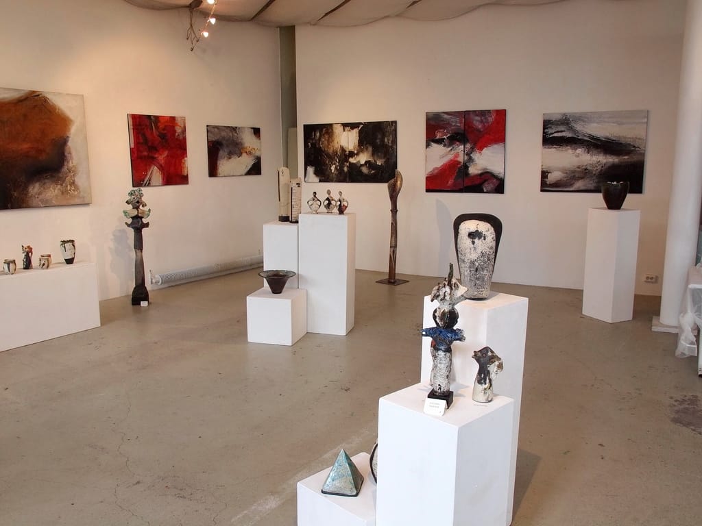The gallery before the opening: large abstract paintings in rust red, black and white hang on the white walls, with ceramic sculptures and vessels on white plinths in front of them